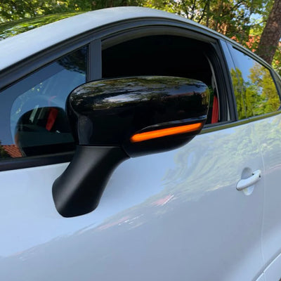 Voiture blanche vue de côté avec rétroviseur noir, clignotant dynamique allumé en orange sous la coque