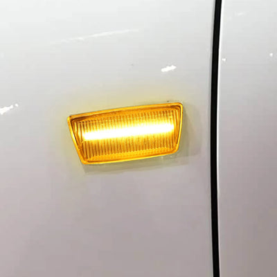 Répétiteur latéral transparent allumé en orange, posé sur une carrosserie blanche