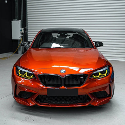 BMW M2 orange de face avec les anneaux jaunes des phares LED allumés