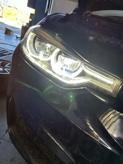 Phare LED monté sur une BMW F30 sombre, anneaux blancs allumés en atelier